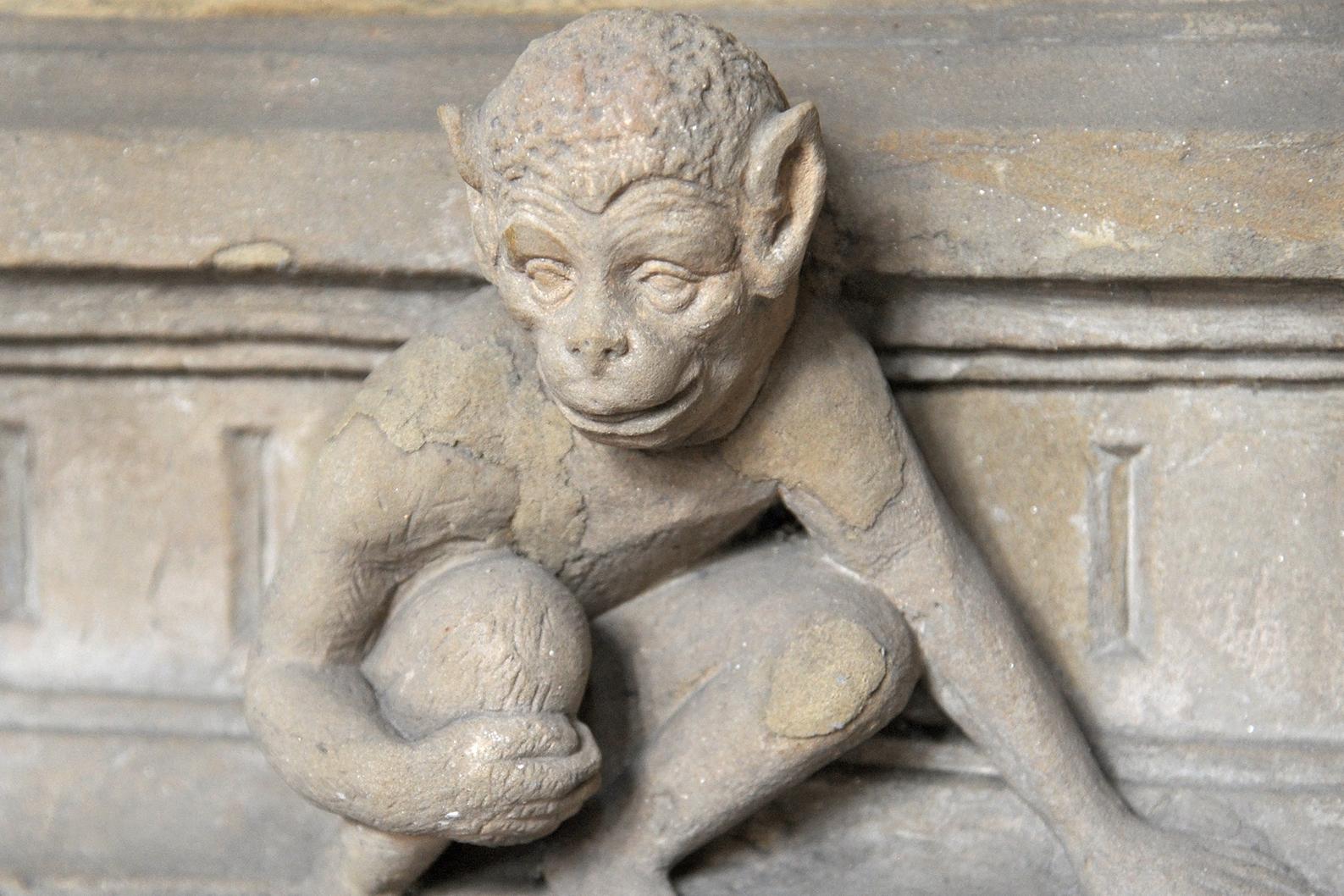 Ein Affe hockt auf einem Sims und stützt sich mit der linken Hand ab