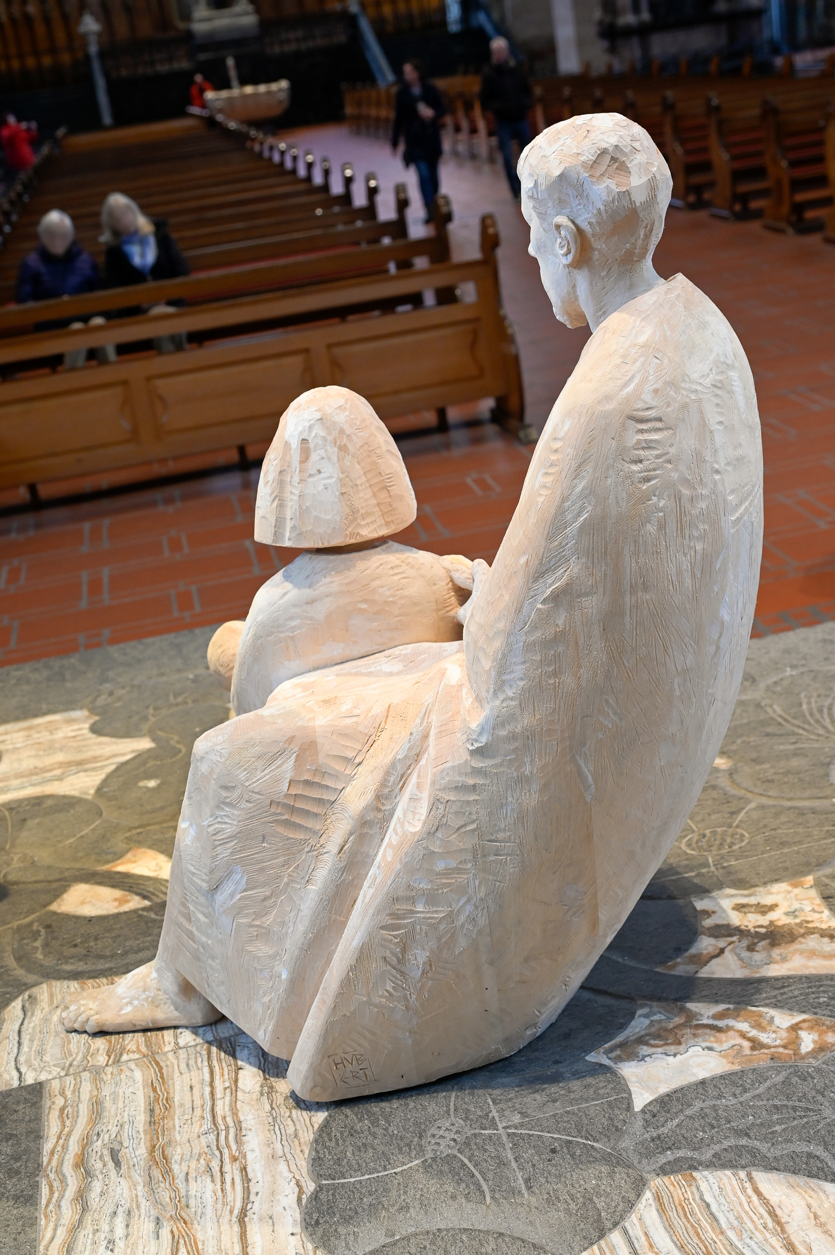 Maria und Josef von hinten fotografiert im Hintergrund betende Menschen